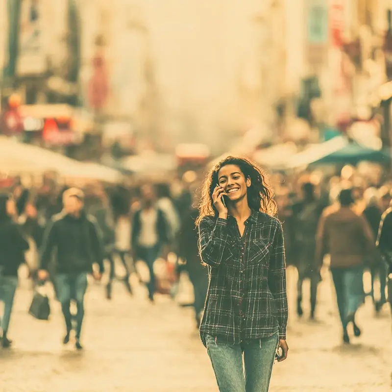 A woman standing on a busy urban street talking on her smartphone
